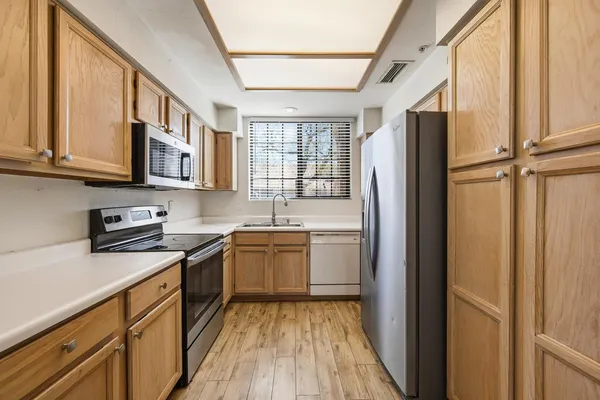 a kitchen with stainless steel appliances granite countertop a refrigerator a sink dishwasher a stove and white countertops with wooden floor