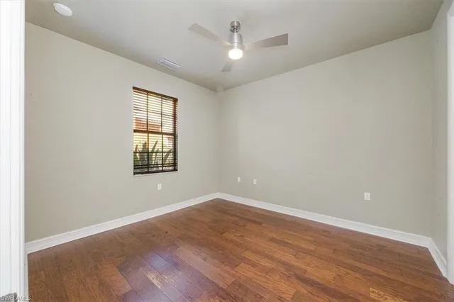 an empty room with wooden floor chandelier fan and windows