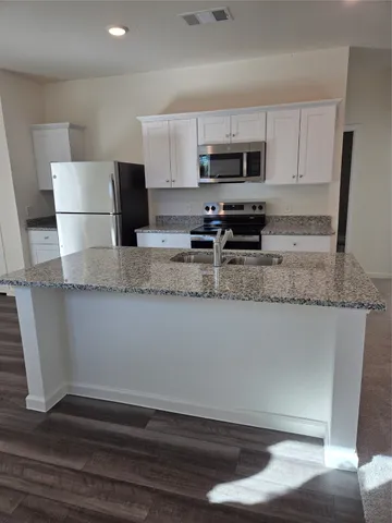 a kitchen with granite countertop a refrigerator a stove a sink and dishwasher with wooden floor