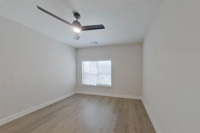 an empty room with wooden floor ceiling fan and windows