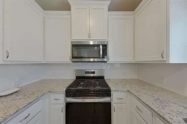 a kitchen with granite countertop white cabinets and a stove top oven
