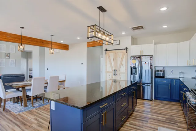 a kitchen with stainless steel appliances granite countertop a refrigerator a sink dishwasher a stove and a dining table with wooden floor