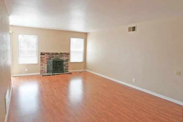 an empty room with wooden floor fireplace and windows