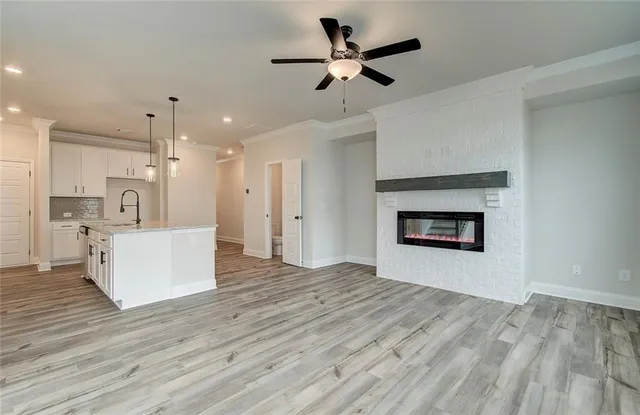 a view of an empty room and kitchen view with wooden floor