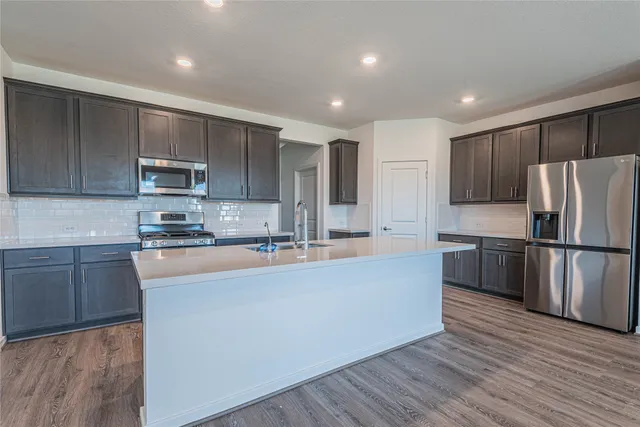 a large kitchen with stainless steel appliances granite countertop a refrigerator a stove a sink and a microwave oven on the wooden floor