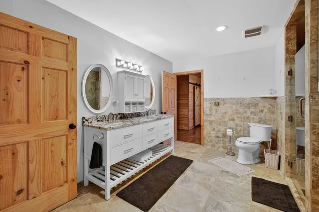 a spacious bathroom with a granite countertop sink a toilet a mirror and shower