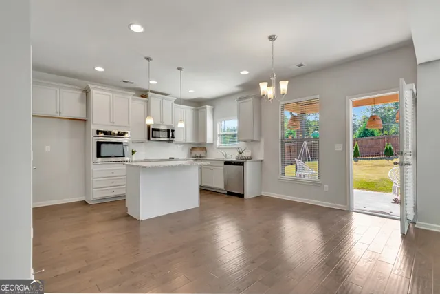 a kitchen with stainless steel appliances granite countertop a refrigerator a sink dishwasher a oven and a dining table with wooden floor