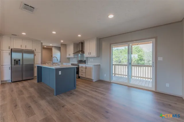 a large kitchen with stainless steel appliances granite countertop a large counter top a wooden floors and a large window