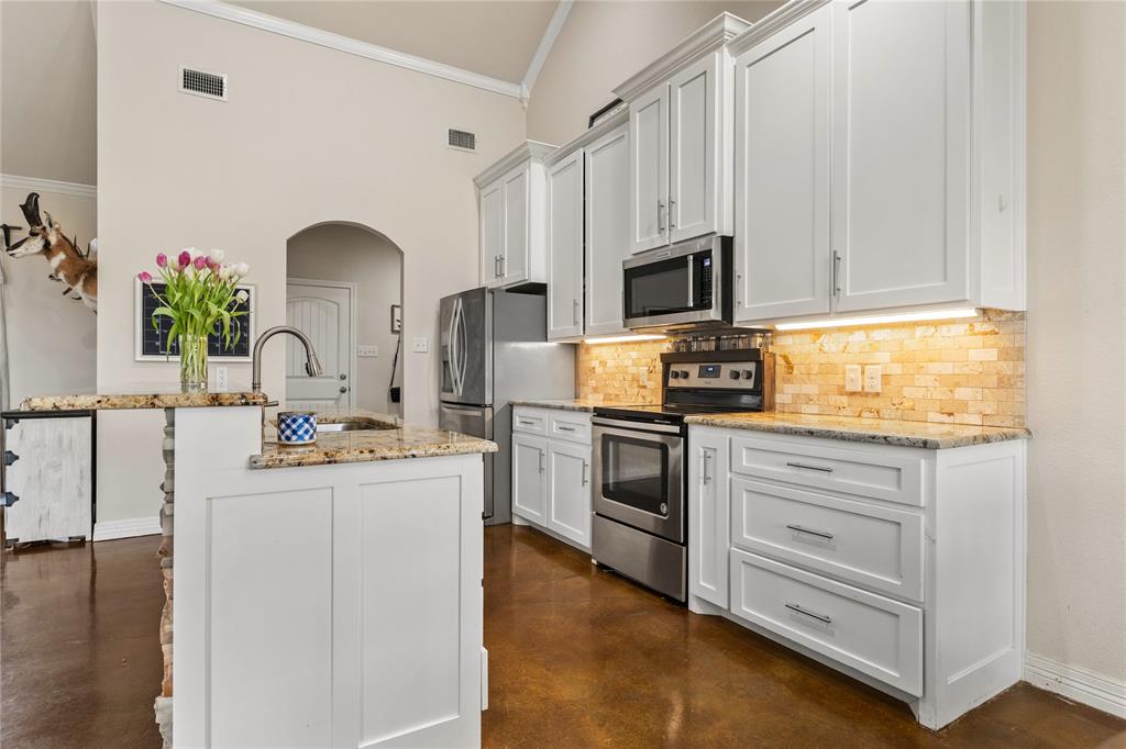 10514 Mesa Drive Waco, TX 76708 - Photo 16 of 37 Kitchen with arched walkways, light stone countertops, appliances with stainless steel finishes, white cabinets, and concrete flooring