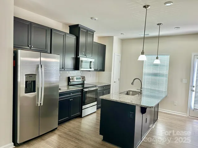 a kitchen with stainless steel appliances granite countertop a refrigerator a sink and wooden floor