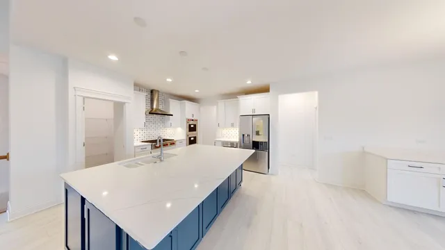 a large white kitchen with a stove a sink a refrigerator and white cabinets with wooden floor