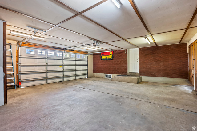 480 North 150 E Street Springville, UT 84663 - Photo 28 of 36 Spacious garage featuring a concrete floor, red brick wall, white overhead door with windows, and fluorescent lighting fixtures
