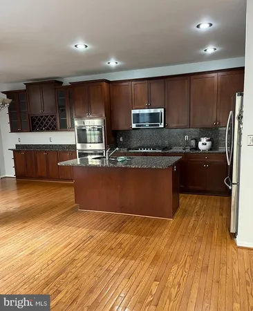 a kitchen with stainless steel appliances granite countertop a refrigerator a sink dishwasher a stove and a microwave oven on the wooden floor