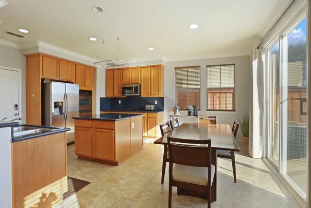 a kitchen with stainless steel appliances granite countertop a stove top oven a sink a dining table and chairs