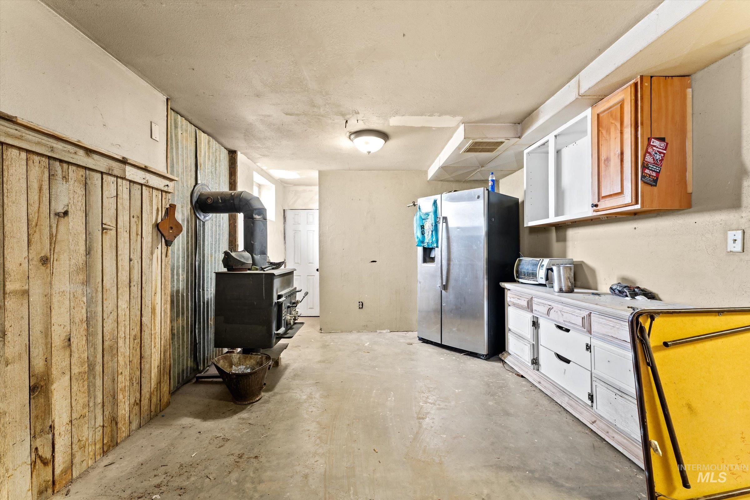 6267 Deer Flat Road Nampa, ID 83686 - Photo 26 of 50 Kitchen with light countertops, a wood stove, stainless steel fridge with ice dispenser, concrete flooring, and wooden walls