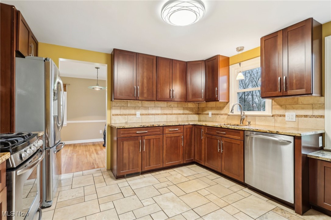 1311 Clearview Road Cleveland, OH 44124 - Photo 12 of 45 Kitchen featuring stainless steel appliances, tasteful backsplash, light stone countertops, and sink