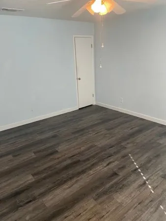a view of an empty room with wooden floor and a chandelier fan