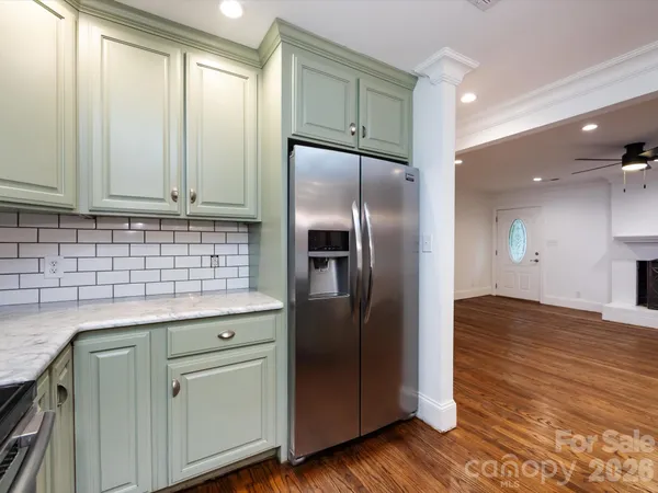 a kitchen with stainless steel appliances granite countertop a refrigerator a sink and white cabinets with wooden floor