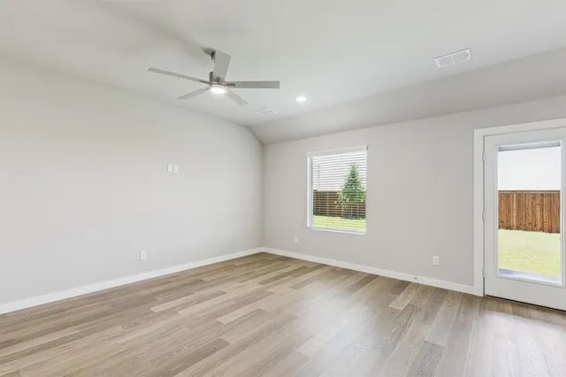 an empty room with wooden floor fan and windows