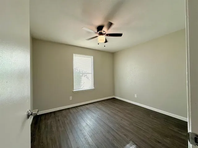 an empty room with wooden floor ceiling fan and windows