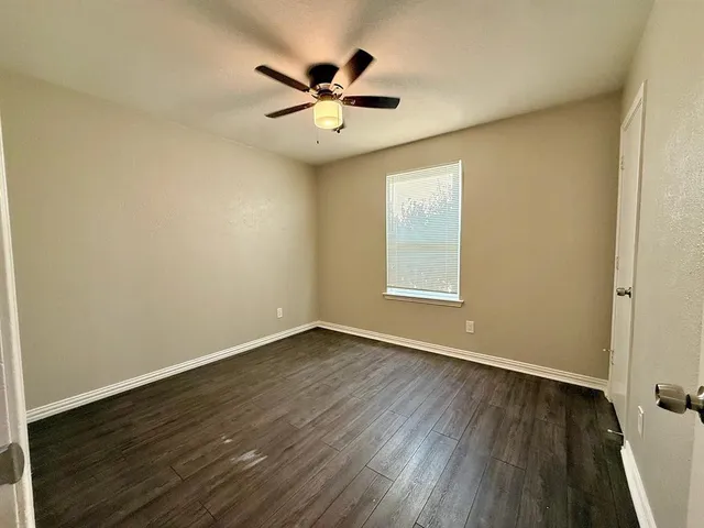 an empty room with wooden floor chandelier fan and windows