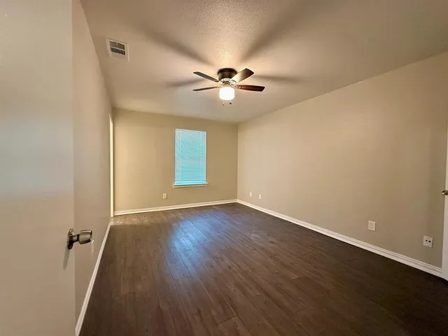 an empty room with wooden floor fan and windows
