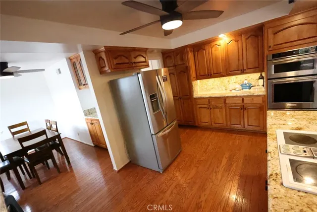 a kitchen with granite countertop a refrigerator a stove a sink and white cabinets with wooden floor