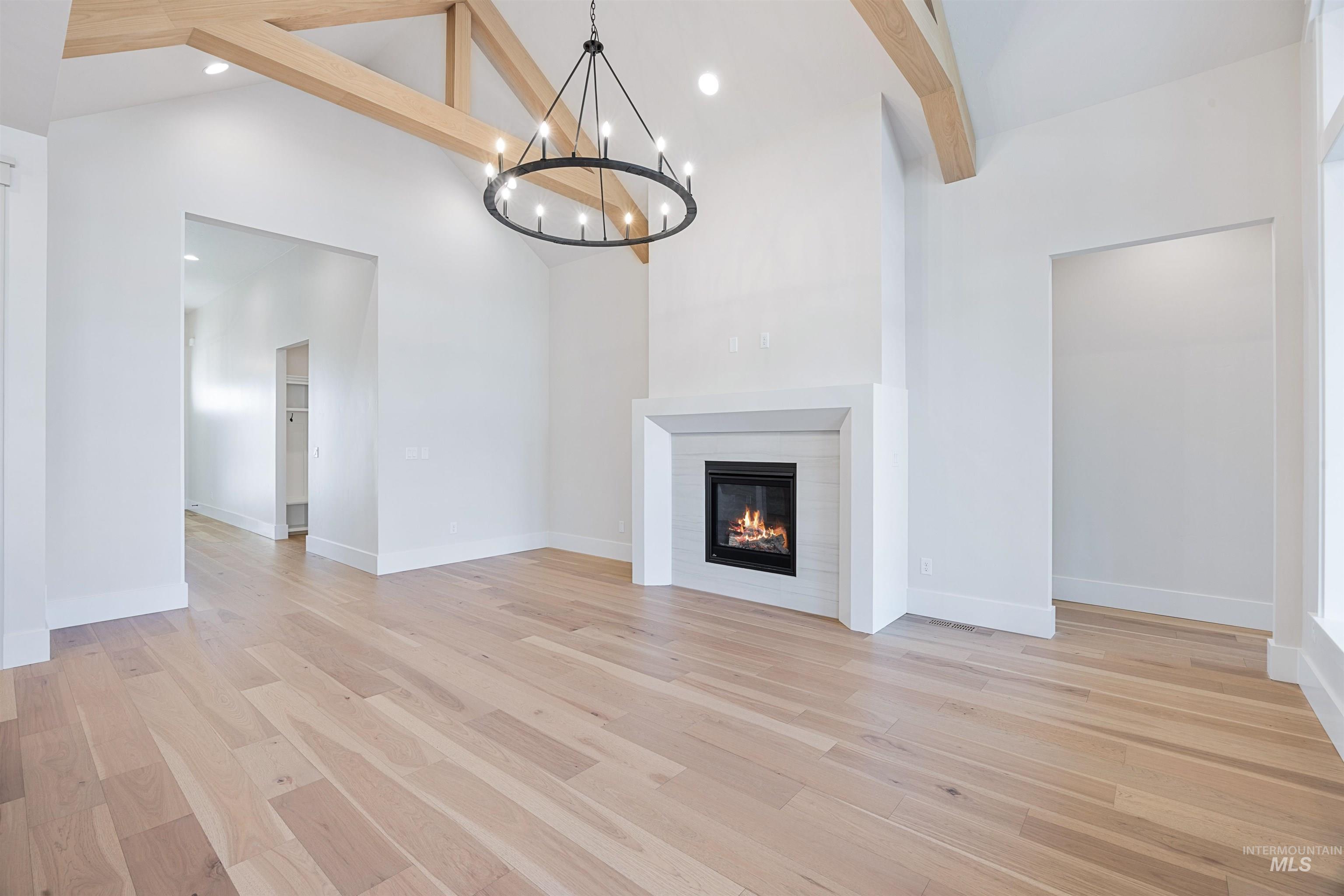 904 East Escalation Street Meridian, ID 83642 - Photo 12 of 36 Vaulted ceiling with exposed wood beams, central fireplace with a white tile surround, wood-finish flooring, recessed lighting, and a circular chandelier