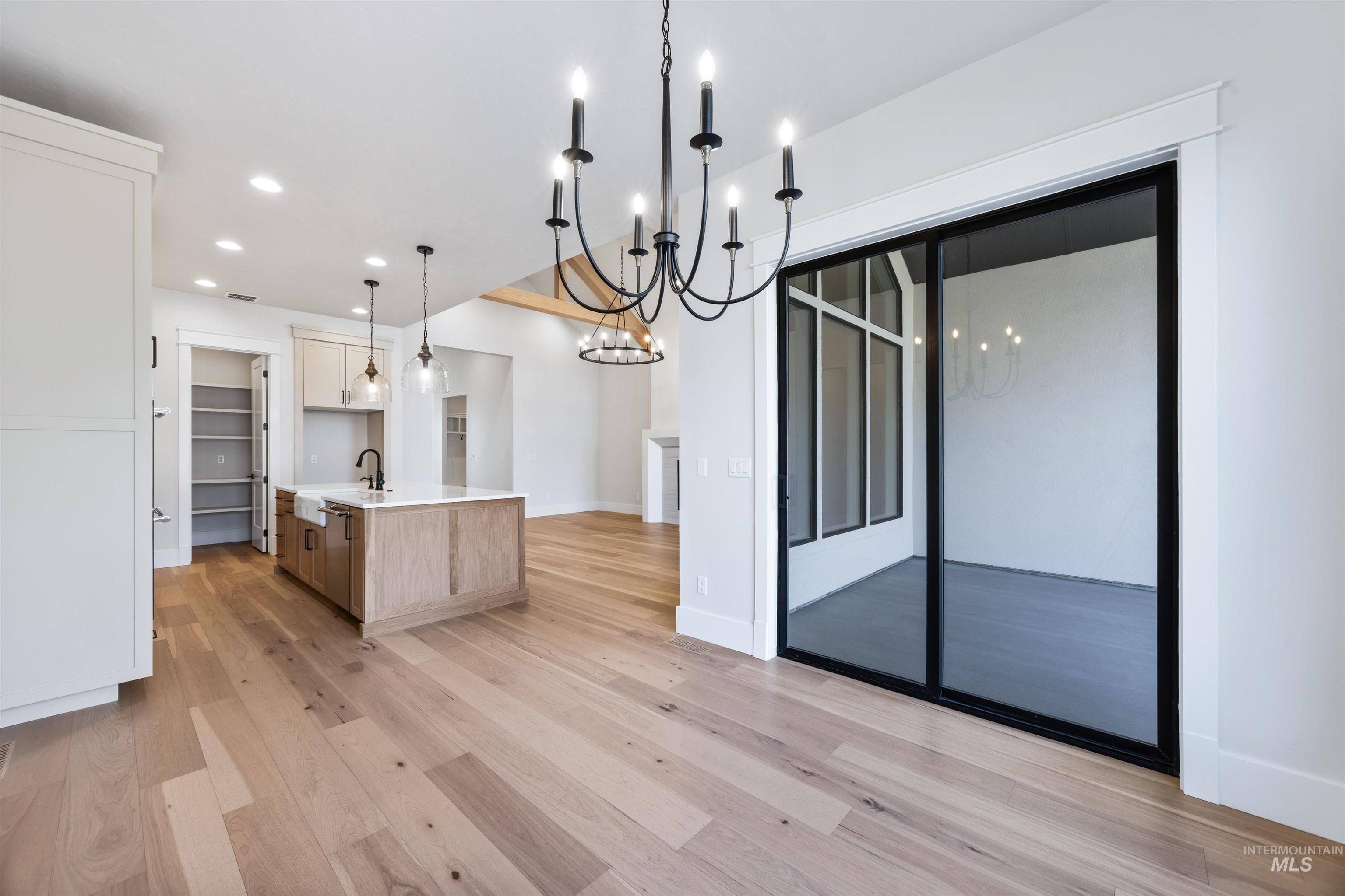 904 East Escalation Street Meridian, ID 83642 - Photo 14 of 36 Spacious interior featuring wide plank wood-finish flooring, a kitchen island with a farmhouse sink, pantry with built-in shelving, and black-framed sliding glass doors