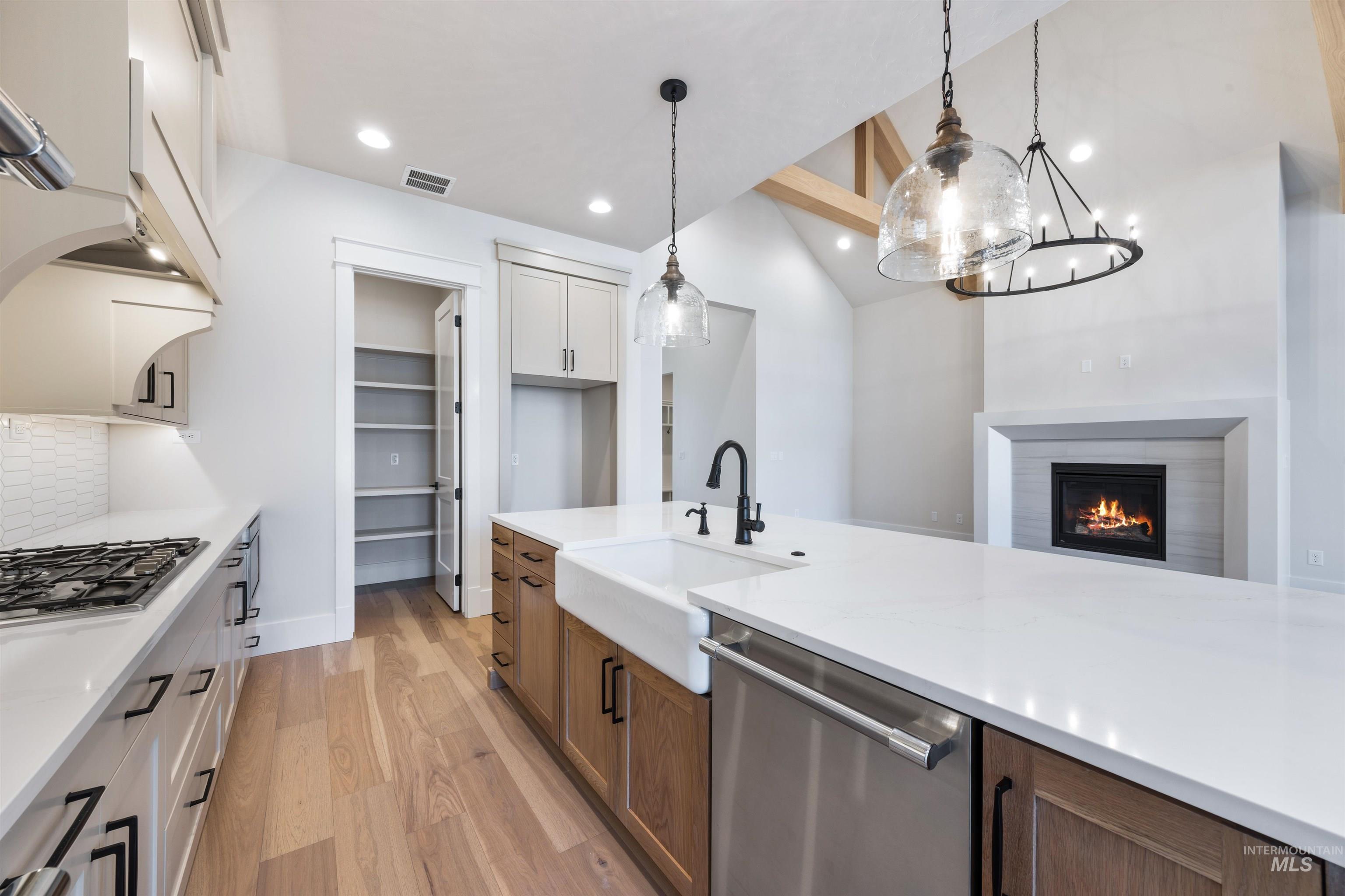 904 East Escalation Street Meridian, ID 83642 - Photo 16 of 36 Open-concept kitchen featuring an island with a farmhouse sink, stainless steel appliances, a gas range with a decorative hood, and light wood-finish flooring