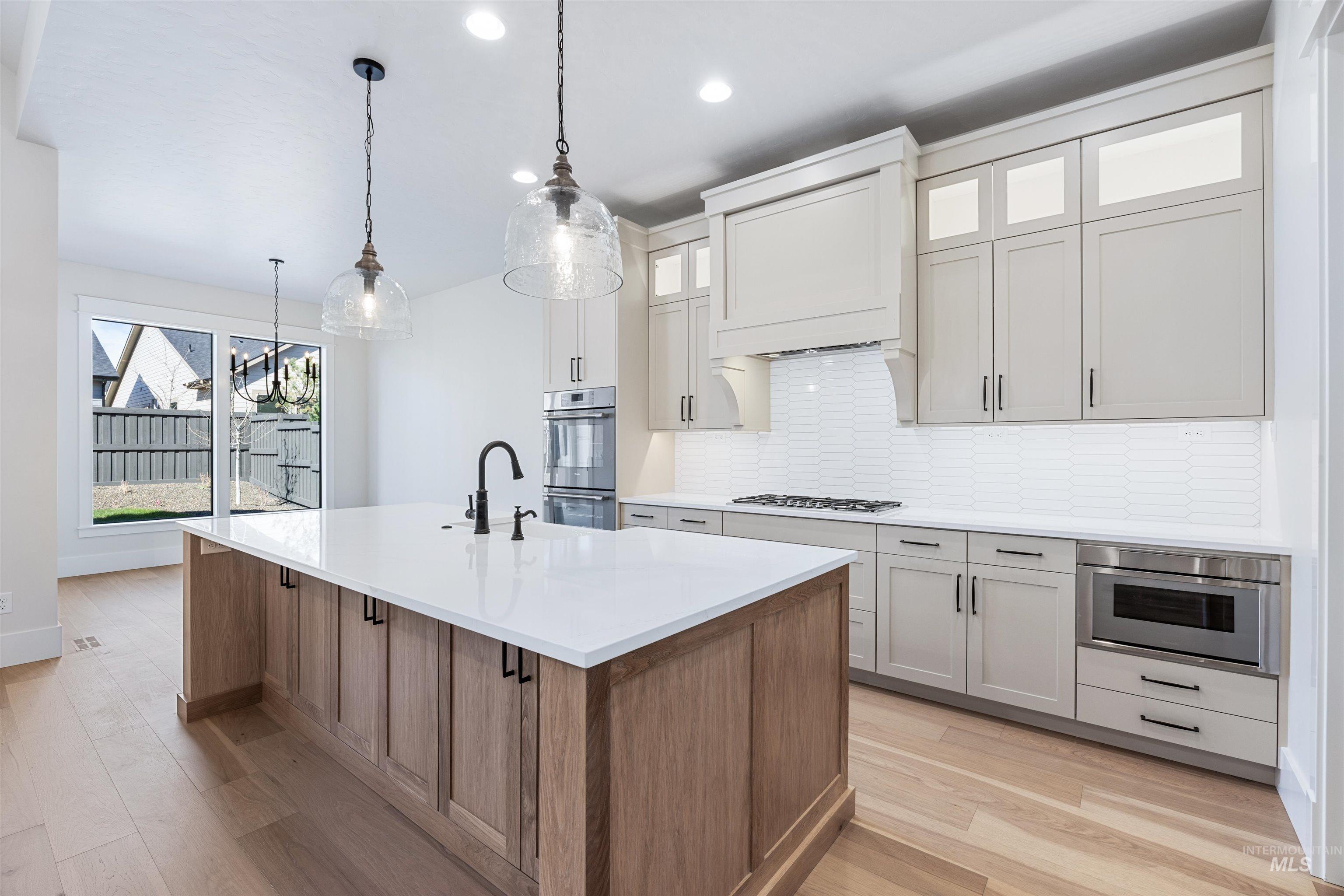 904 East Escalation Street Meridian, ID 83642 - Photo 19 of 36 Gourmet kitchen featuring a large central island with a solid surface countertop, light wood-finish cabinetry, built-in stainless steel appliances, a white subway tile backsplash, and light wood-finish flooring