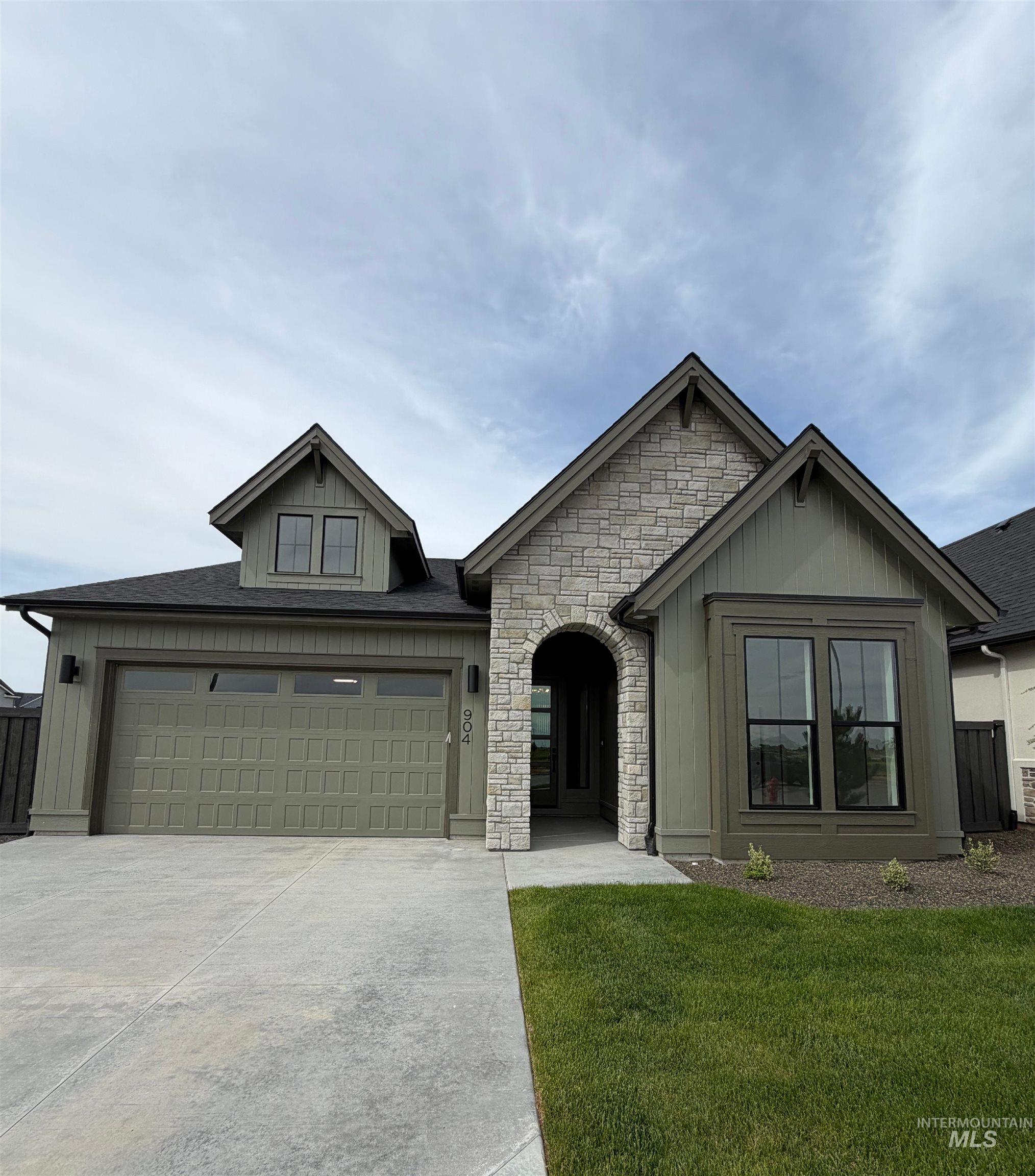 904 East Escalation Street Meridian, ID 83642 - Photo 2 of 36 Craftsman-style exterior featuring a stone facade, arched entry, board and batten siding, dark framed windows, and an integrated garage