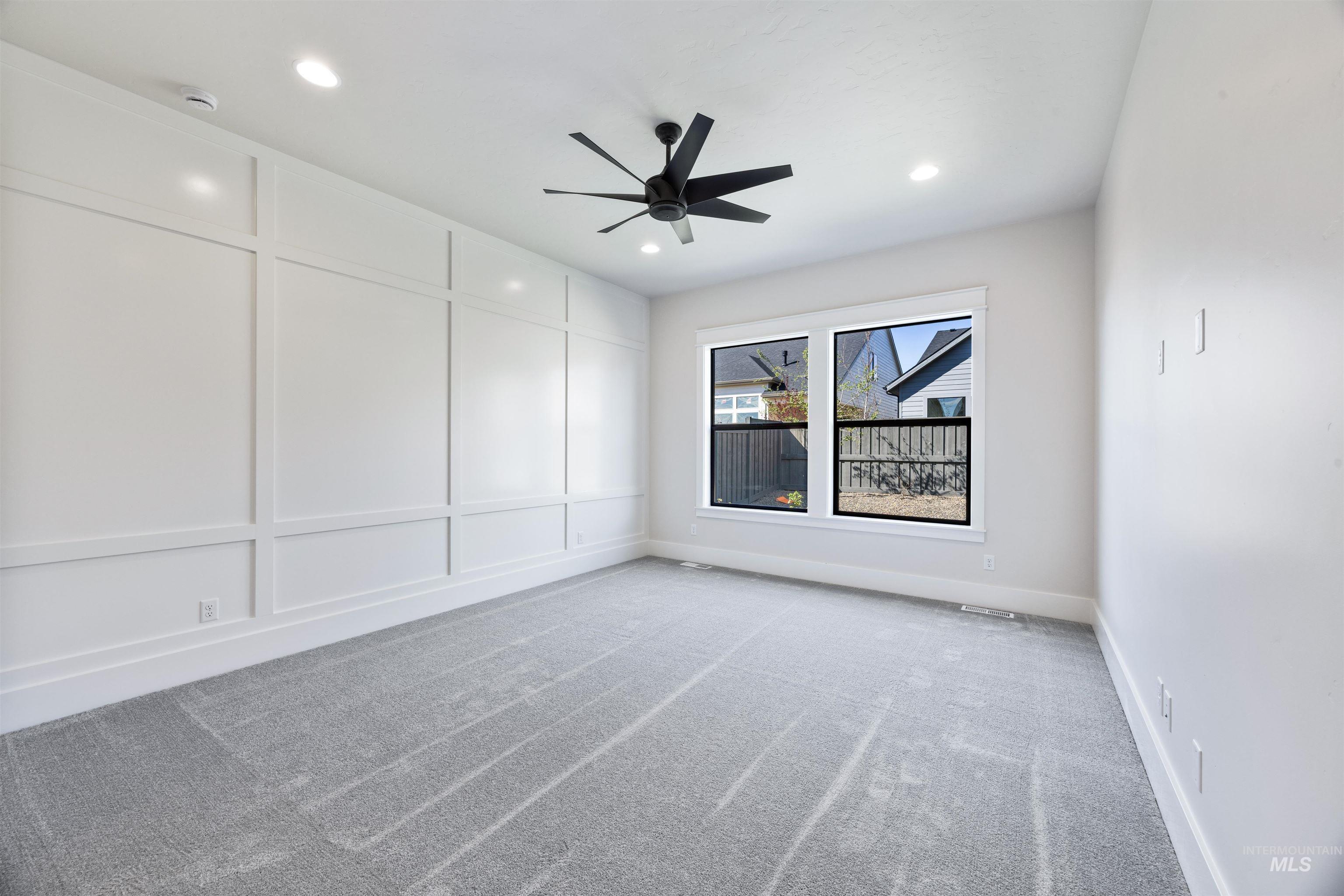904 East Escalation Street Meridian, ID 83642 - Photo 27 of 36 Spacious room featuring a decorative accent wall with panel molding, dual windows with black trim, recessed lighting, and a contemporary ceiling fan