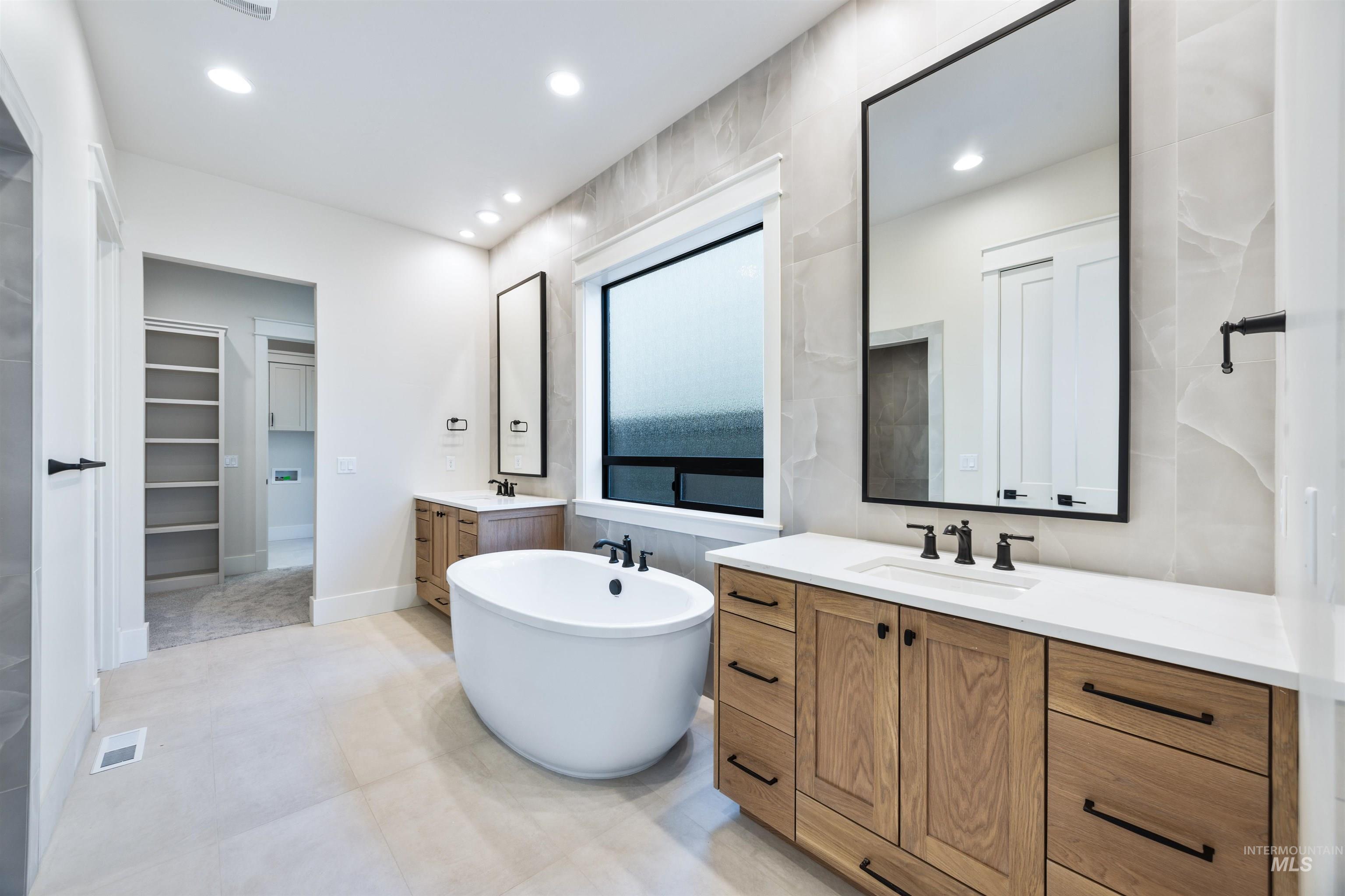 904 East Escalation Street Meridian, ID 83642 - Photo 29 of 36 Spacious bathroom featuring a freestanding soaking tub, dual wood-finish vanities with white countertops, matte black plumbing fixtures, and large-format wall tiles