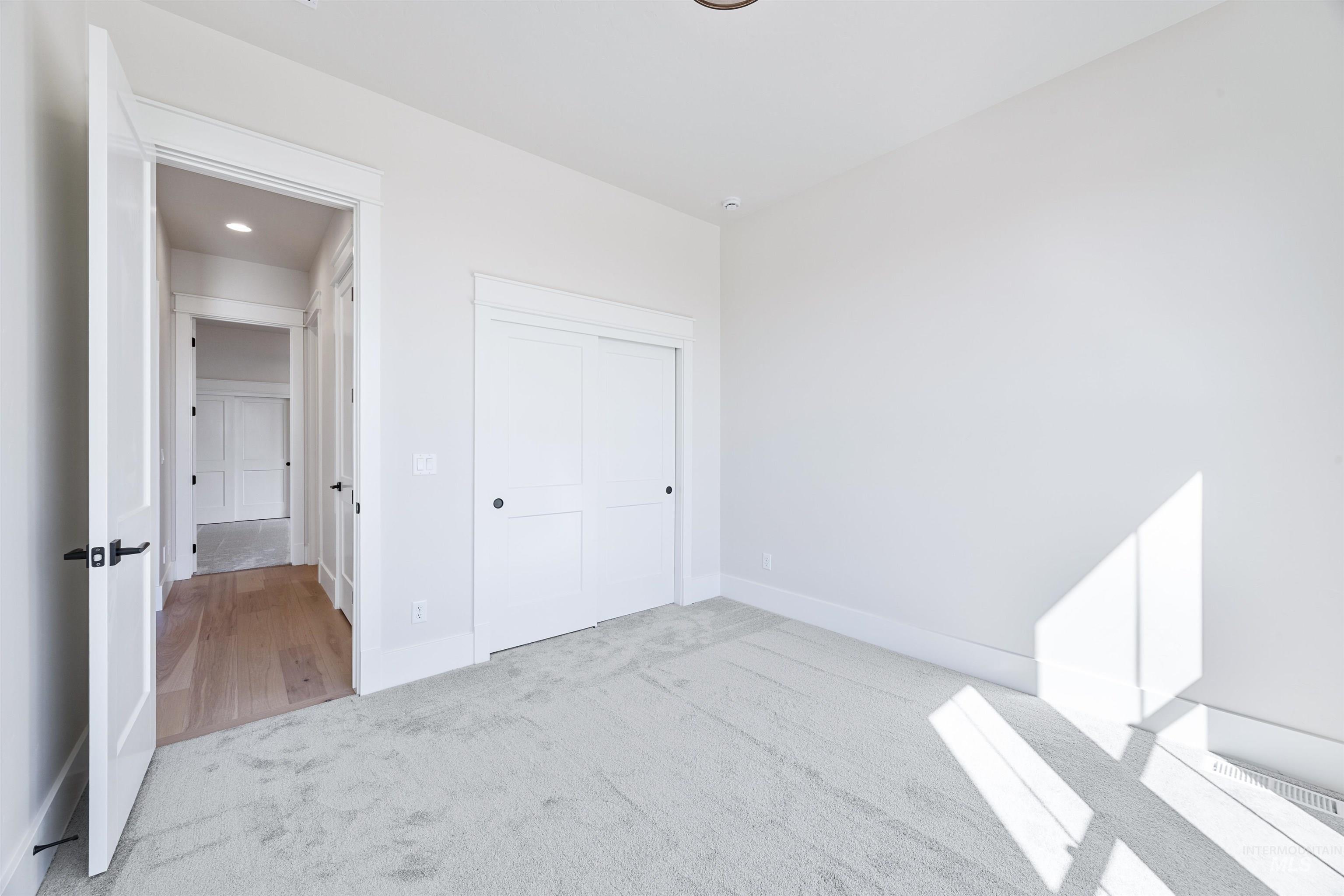 904 East Escalation Street Meridian, ID 83642 - Photo 5 of 36 Carpeted room with white walls, a built-in closet with sliding panel doors, and a doorway opening to a wood-finish flooring hallway