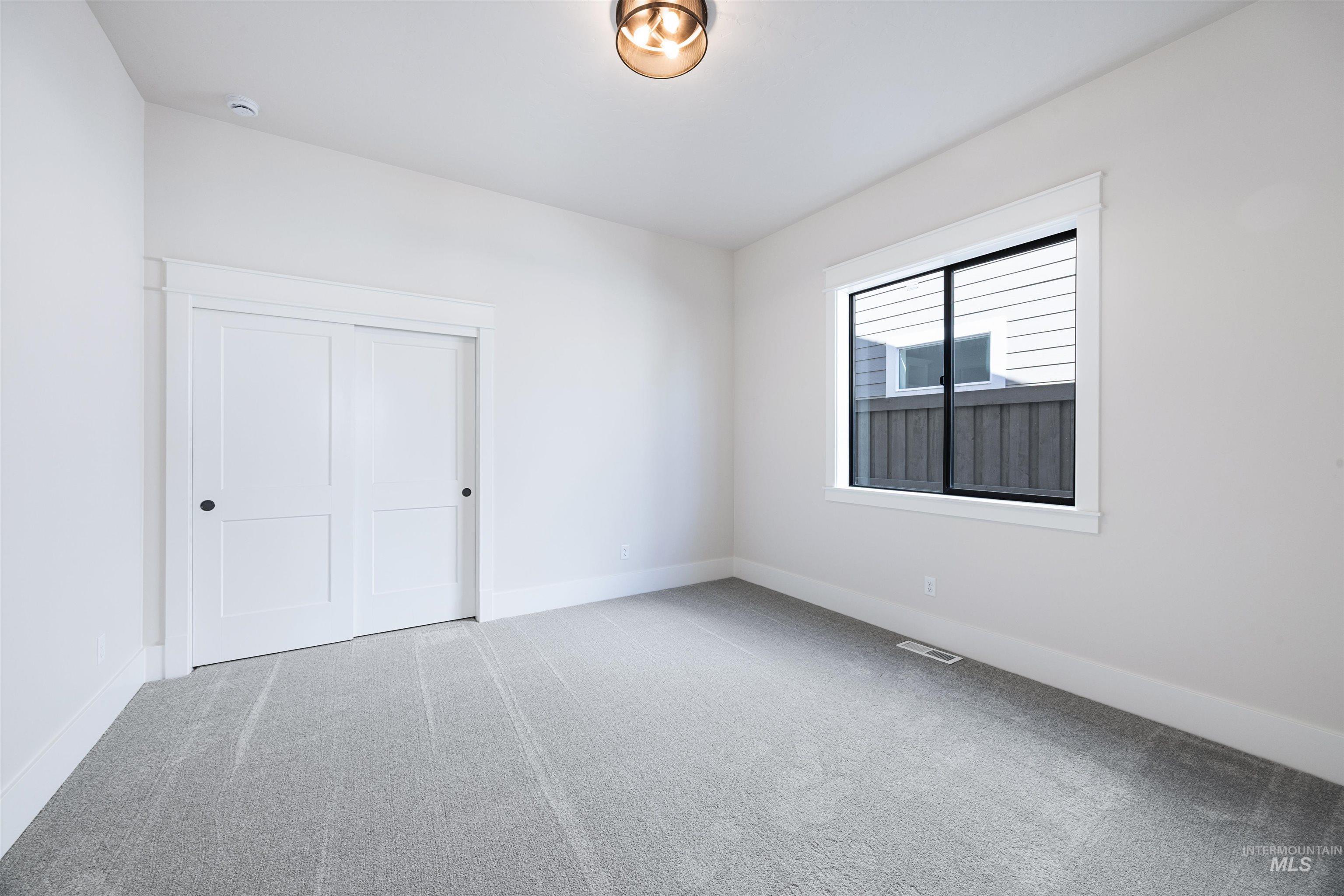 904 East Escalation Street Meridian, ID 83642 - Photo 7 of 36 Bright interior space featuring a window with black trim, a flush-mount ceiling light fixture, sliding white panel doors, and gray carpeting