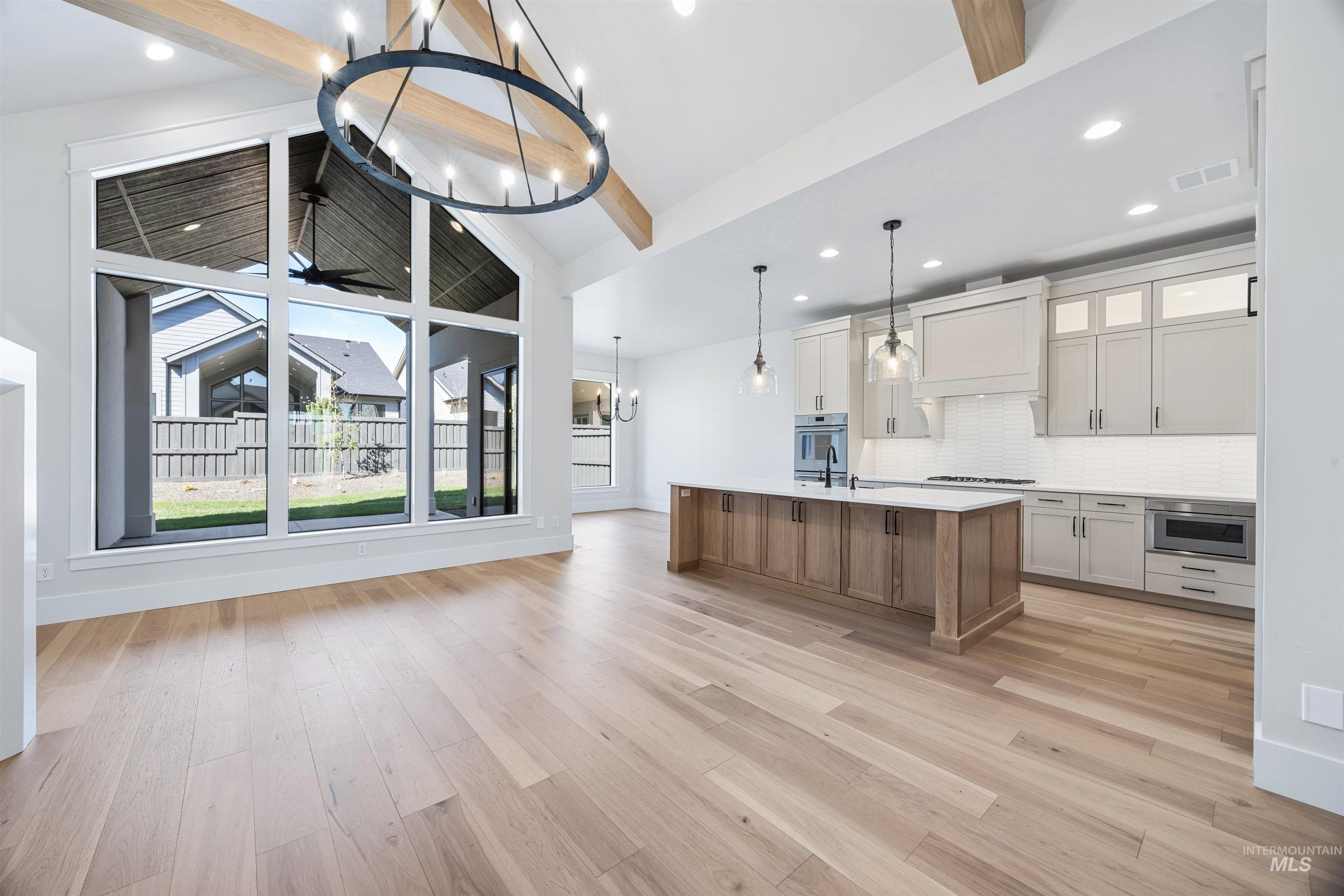 904 East Escalation Street Meridian, ID 83642 - Photo 10 of 36 Open-concept living space featuring vaulted ceilings with exposed wood beams, a large circular chandelier, and light wood-finish flooring