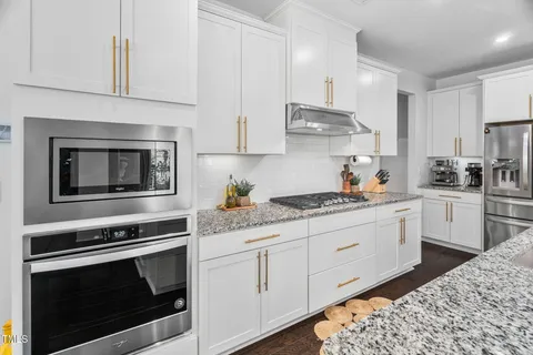 a kitchen with stainless steel appliances kitchen island granite countertop a dining table chairs and white cabinets