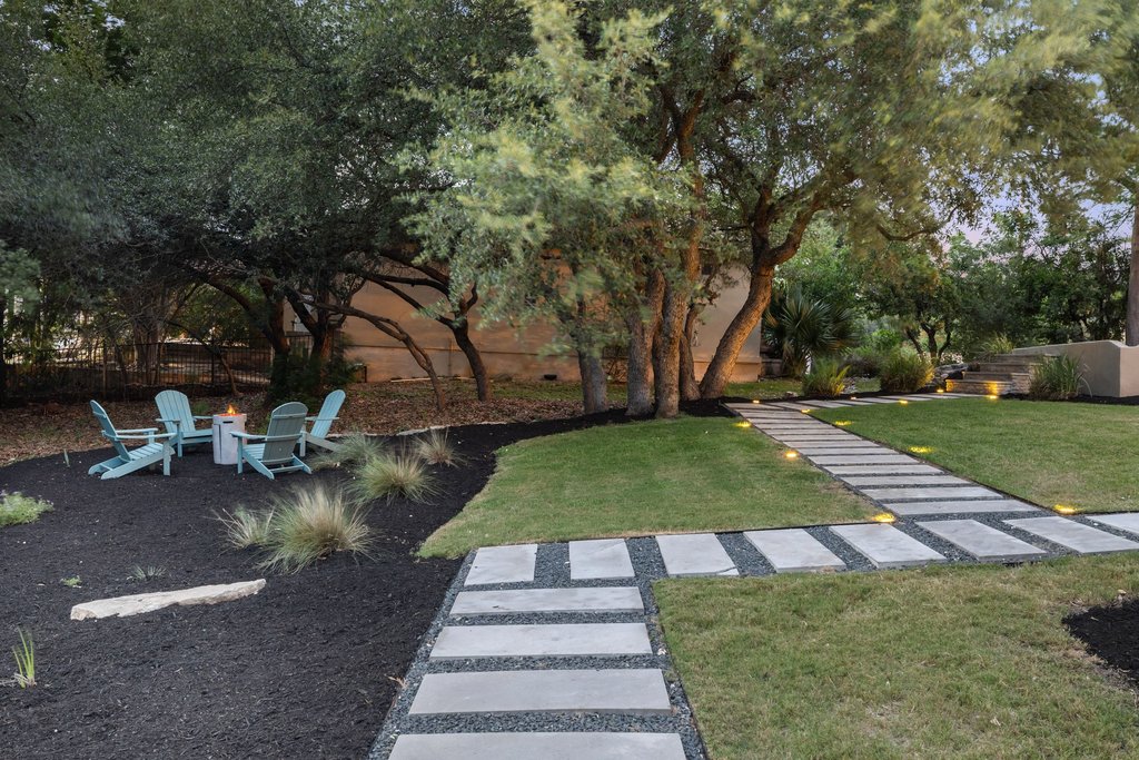 701 Hurst Creek Road Lakeway, TX 78734 - Photo 28 of 37 Landscaped backyard featuring a stone paver pathway, manicured lawn, and mature trees with a firepit seating area.