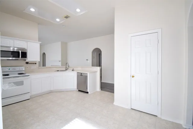 a large white kitchen with a sink and dishwasher a stove top oven with white cabinets