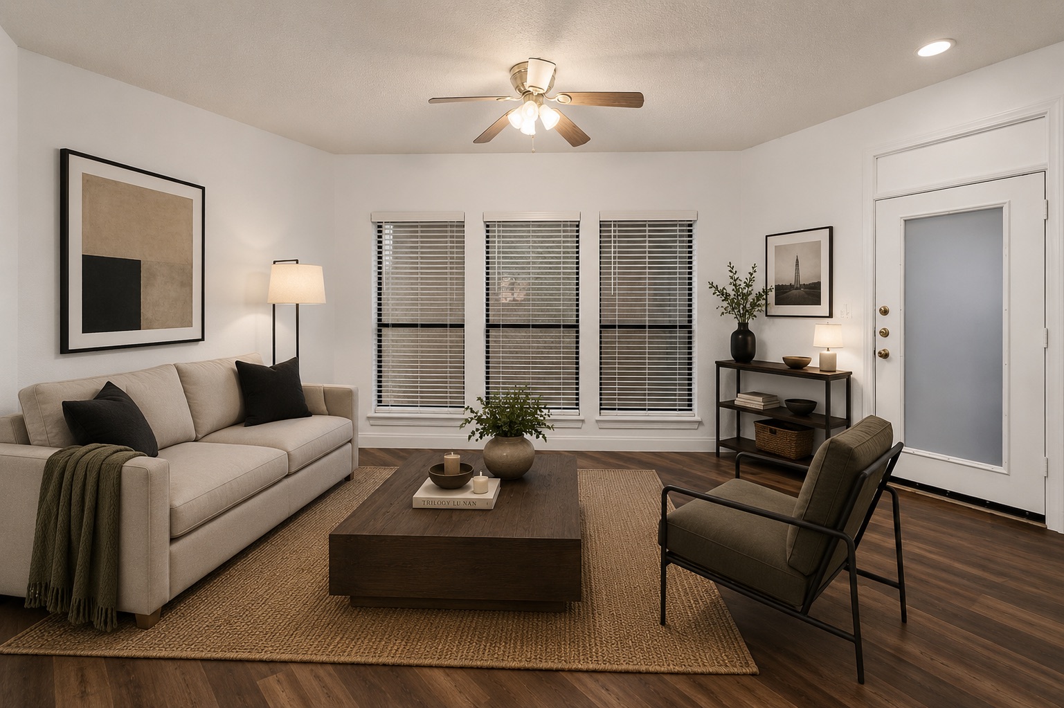 Spacious living area featuring wood-finish flooring, a ceiling fan with integrated lighting, and white walls. Virtually staged.