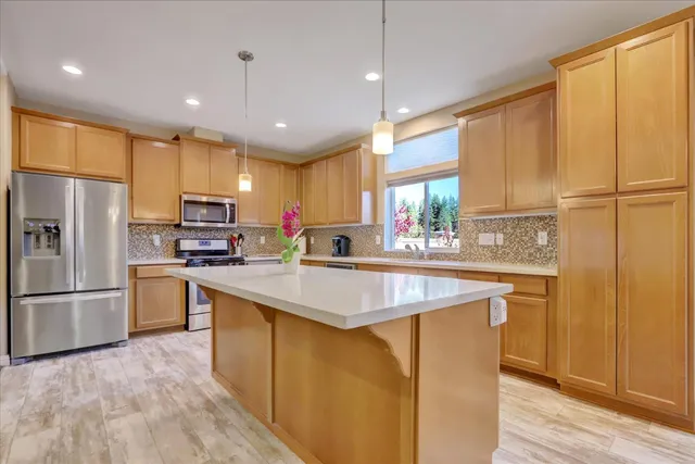 a kitchen with stainless steel appliances granite countertop a refrigerator a sink dishwasher a s stove top oven a large island with wooden floor and cabinets
