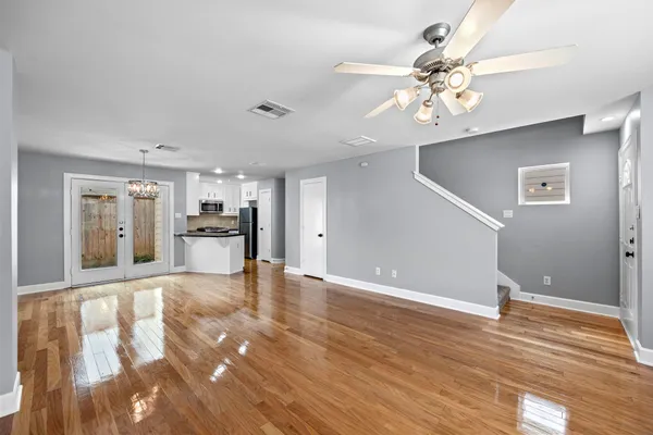 a view of an empty room with wooden floor and a kitchen