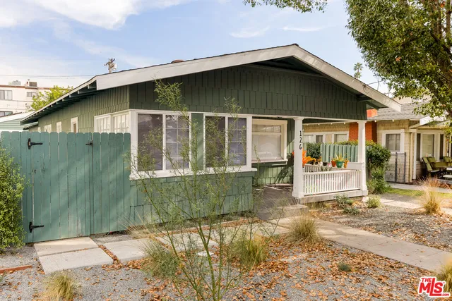 a view of a white house with a large tree and wooden fence