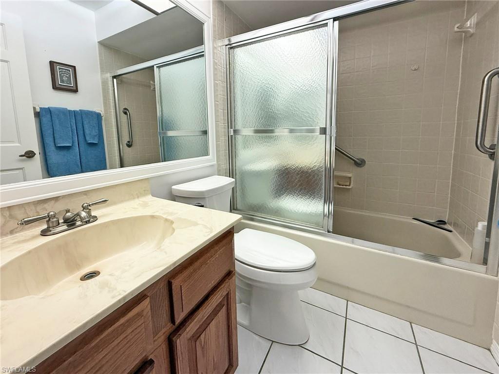 2005 Pine Isle Lane, Unit 2005 Naples, FL 34112 - Photo 11 of 23 Full guest bath featuring an oak vanity, shower / bath combination with glass door, and light tile floor.