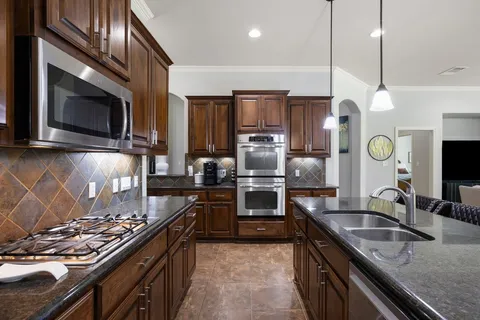 a kitchen with stainless steel appliances granite countertop a sink a stove top oven a refrigerator with wooden cabinets and floor