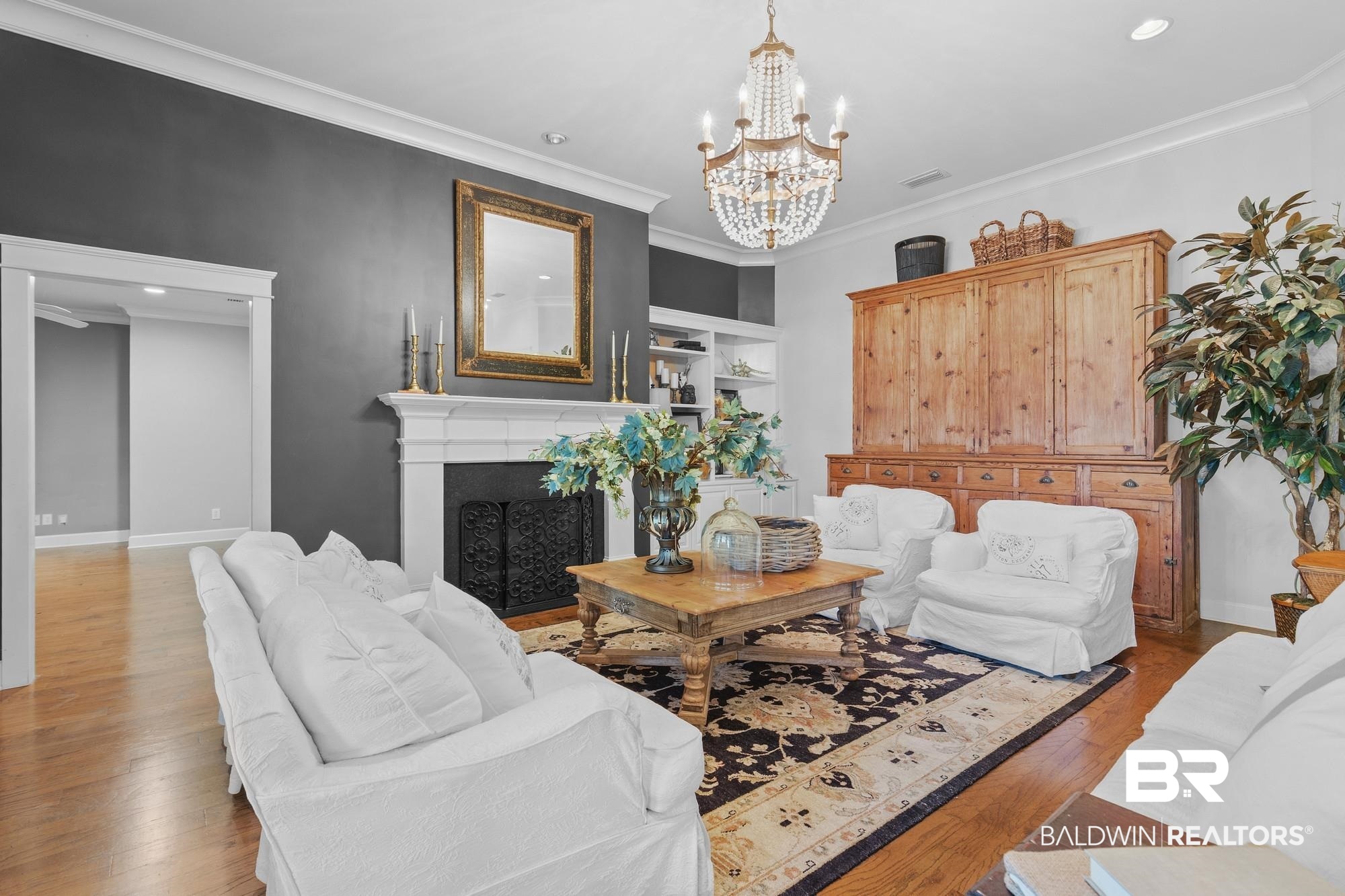 11261 Halcyon Loop Daphne, AL 36526 - Photo 6 of 41 Spacious room featuring hardwood flooring, a white mantel fireplace with a decorative screen, built-in shelving, crown molding, and a crystal chandelier