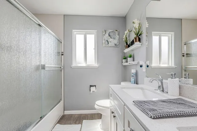 a bathroom with a granite countertop sink a toilet a window and shower