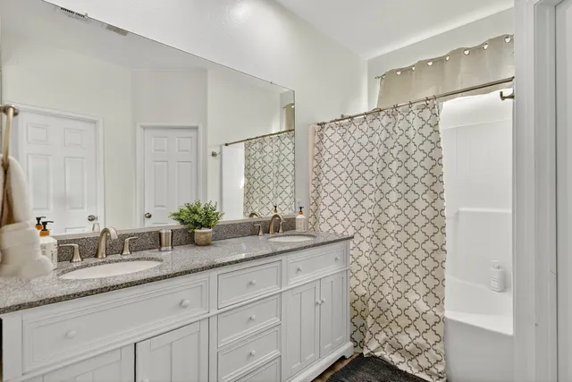 a bathroom with a granite countertop sink a mirror a shower and a double vanity