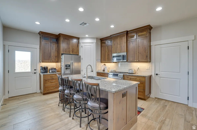 217 West Terrace Circle Toquerville, UT 84774 - Photo 3 of 25 Kitchen featuring light stone counters, a kitchen bar, stainless steel appliances, a center island with sink, and light wood-style flooring